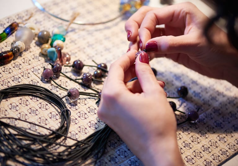 Artesano joyero ensartando cuentas de vidrio moradas en un collar de cordón negro hecho a mano.