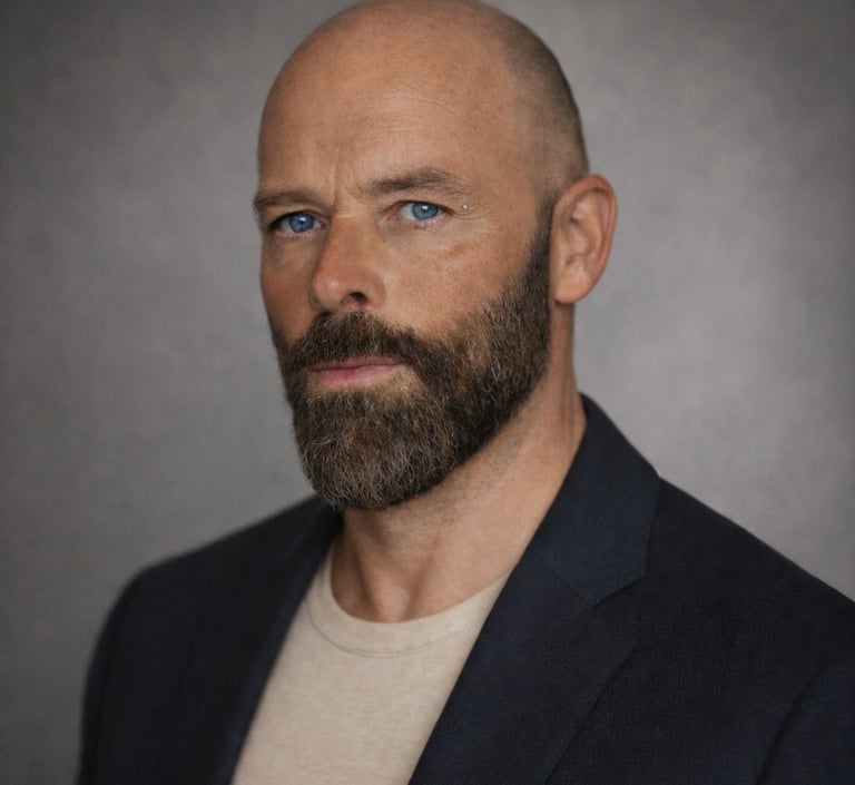 Professional headshot of Damon with blue eyes and a groomed beard wearing a dark blazer.