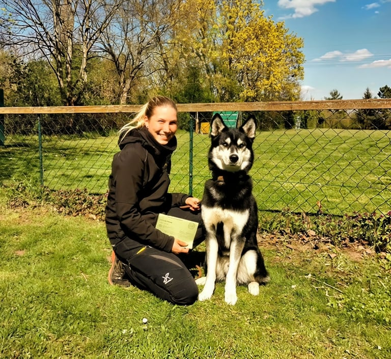A smiling woman posing with her Alaskan Husky dog at an outdoor obedience training school.
