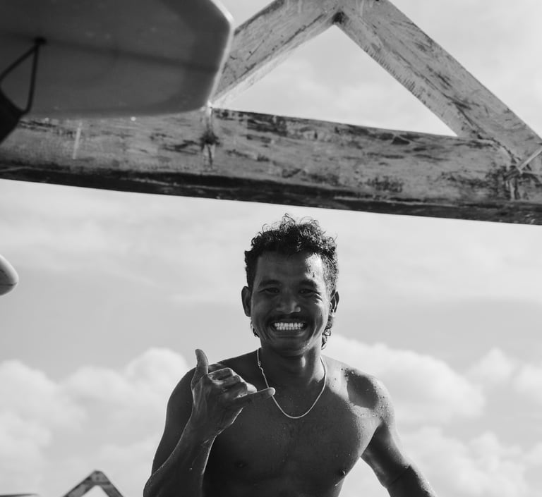 Black and white photo of the surf school owner on his surfboard showing a shaka gesture.