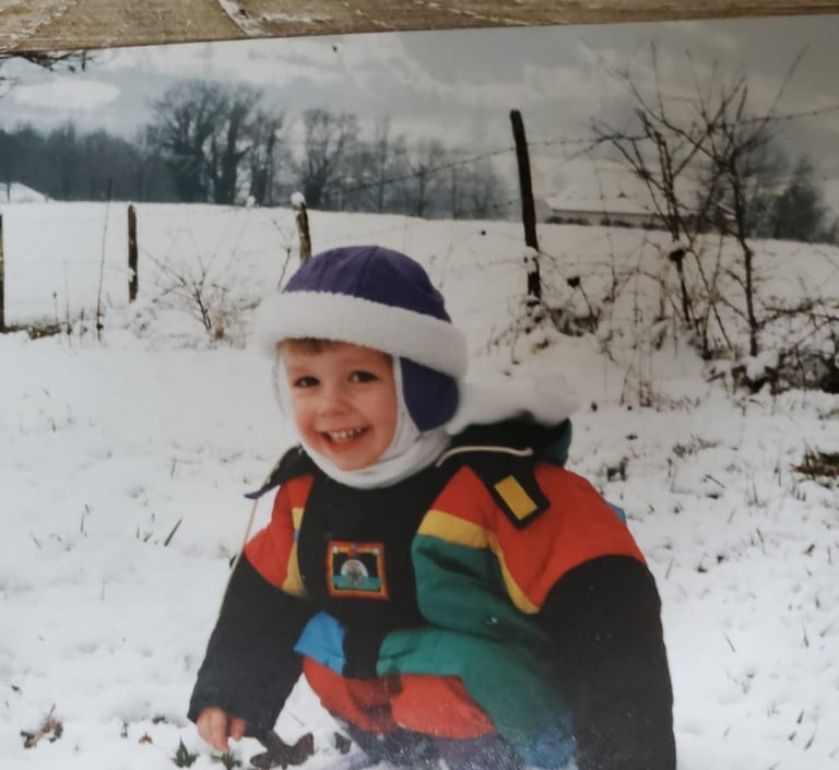 Monsieur rêve enfant, vêtu d'une veste d'hiver colorée et d'un bonnet violet, joue dans un champ
