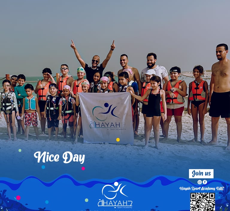 Children and instructors from Hayah Sport Academy UAE posing on a beach in swimming gear.