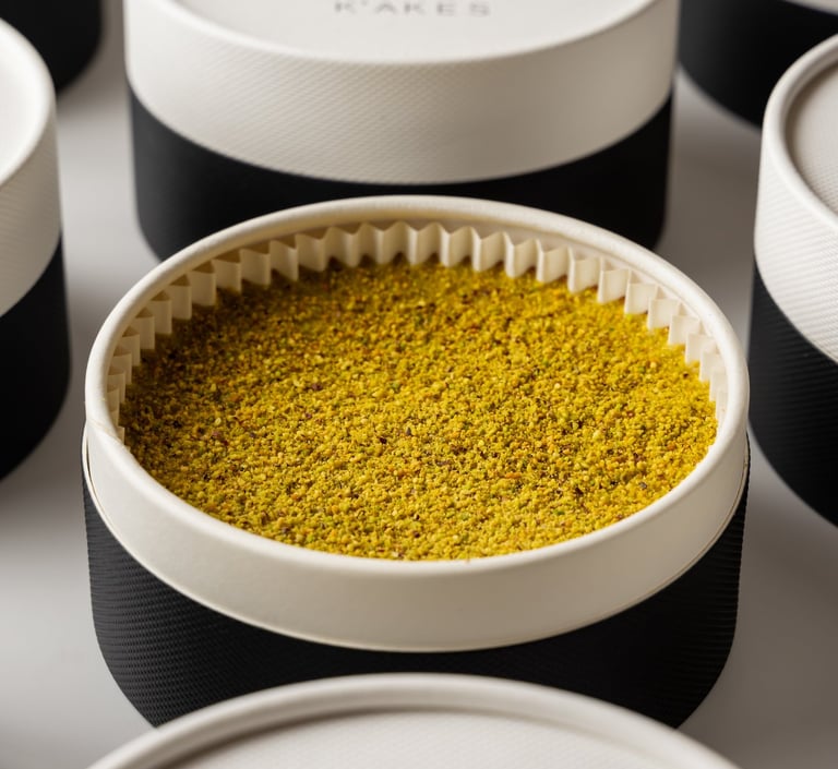 Elegant round gift boxes of K'AKES gourmet treats featuring crushed pistachio toppings.