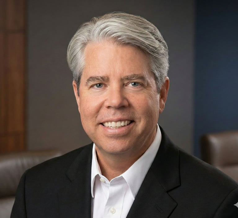 Professional headshot of a smiling male executive with grey hair in a black suit jacket.