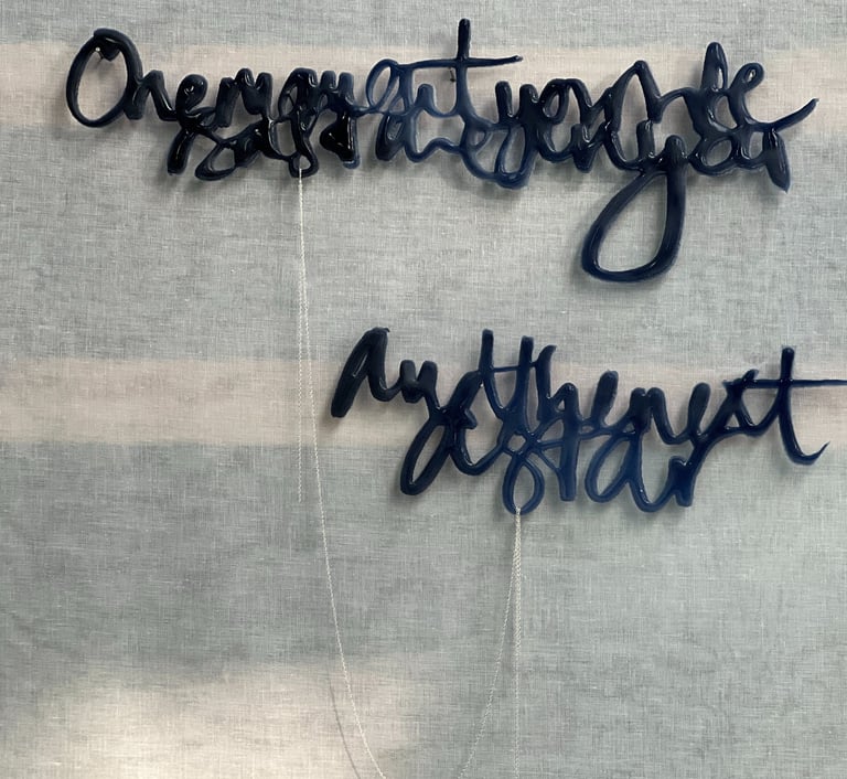 Two lines of semi-abstract text, made in glass and joined by a silver rope chain.