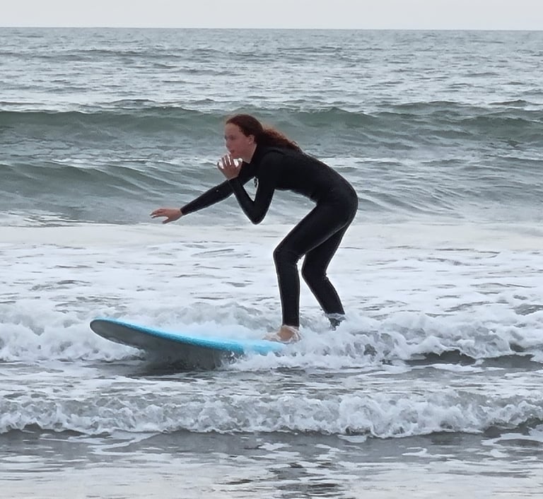 A female surfer riding a baby blue surfboard and a small broken wave.
