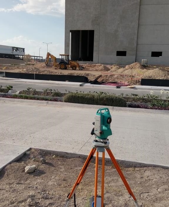 A digital total station on a tripod performing land surveying at a commercial building construction site.
