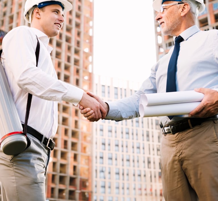 Bir şantiye alanında birbirinden memnun olan ve el sıkışan iki adamın fotoğrafı.