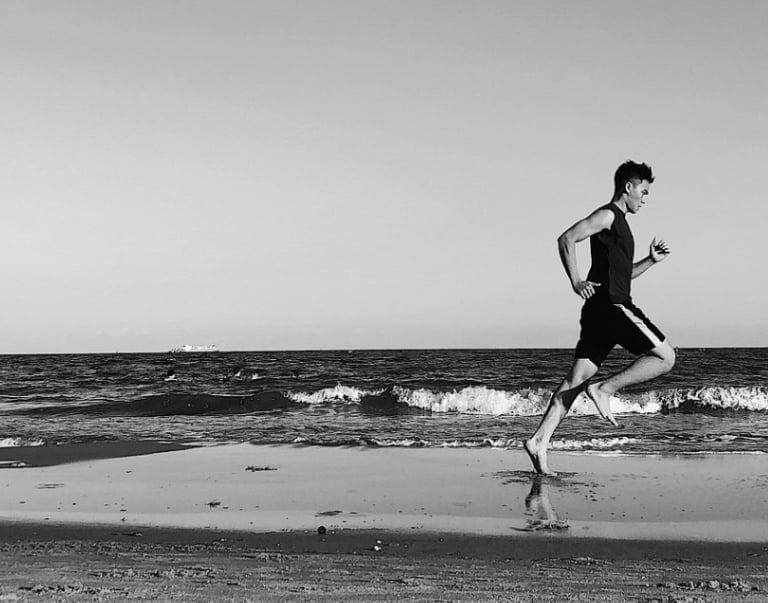 a man running on the beach with a surfboard
