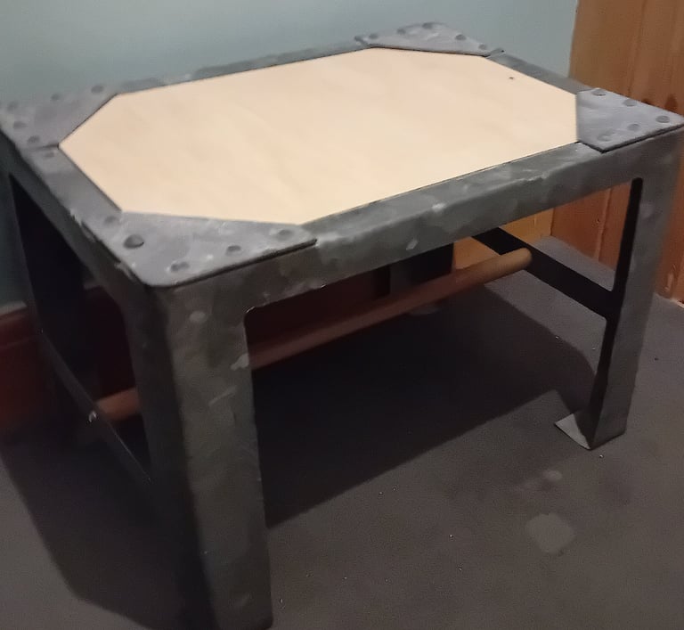 A plywood top has been added under the rivetted corners and wooden bar joining the 2 pairs of legs