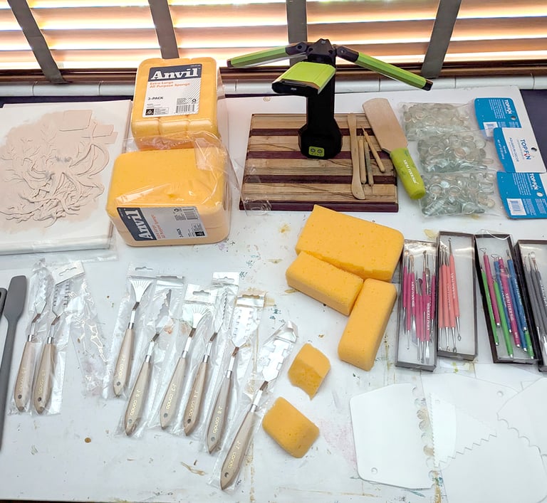 Art artist's drawing table filled with sculpture relief tools, sponges, clay sculpting tools, silicone kitchen spatulas.