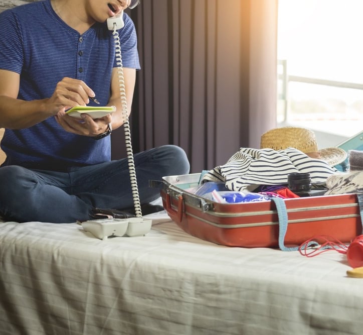 a man sitting on a bed with a suitcase and a phone