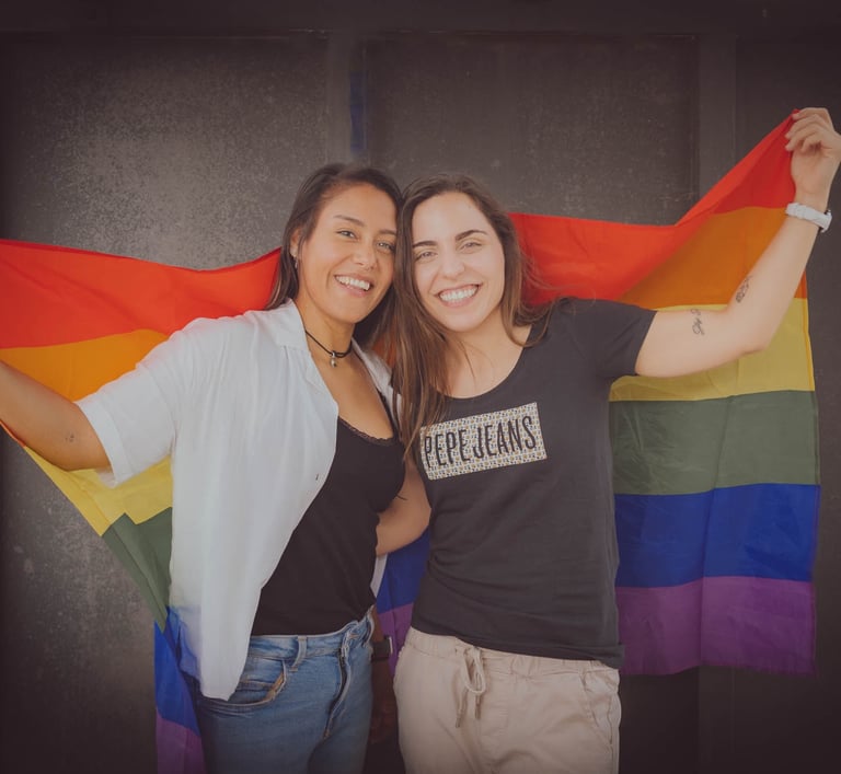 "Pareja lesbiana celebrando su amor con la bandera LGBTQ+ en un evento de orgullo."