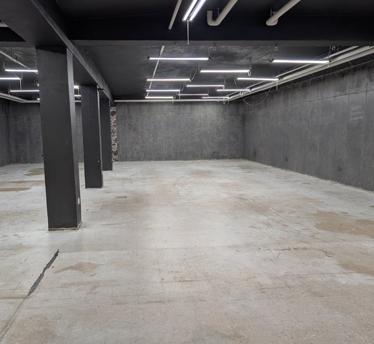Large well lit basement studio with a concrete floor and grey walls
