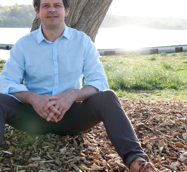 Un homme souriant qui pose, adossé à un arbre
