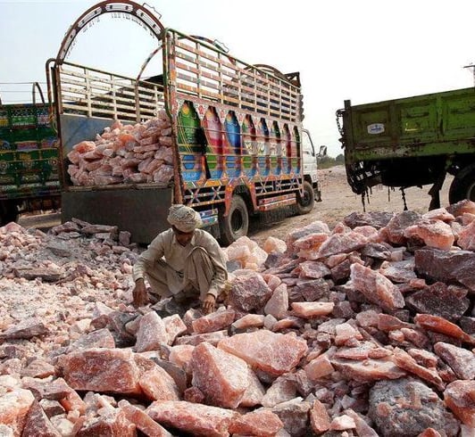 A worker sorts raw Himalayan pink salt rocks near transport trucks at a salt mining site in Pakistan