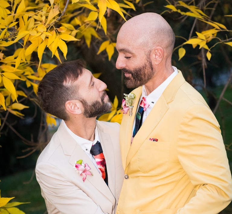 Pareja de hombres gay casados con ropa colorida, mirándose enamorados. Bodas LGBTQ+ en España."