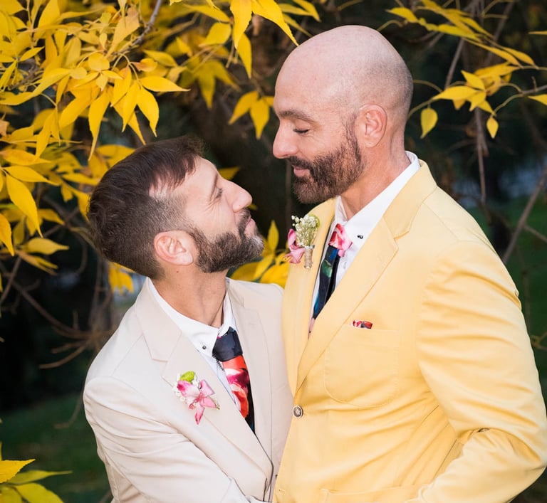 Pareja de hombres gay casados con ropa colorida, mirándose enamorados. Bodas LGBTQ+ en España."
