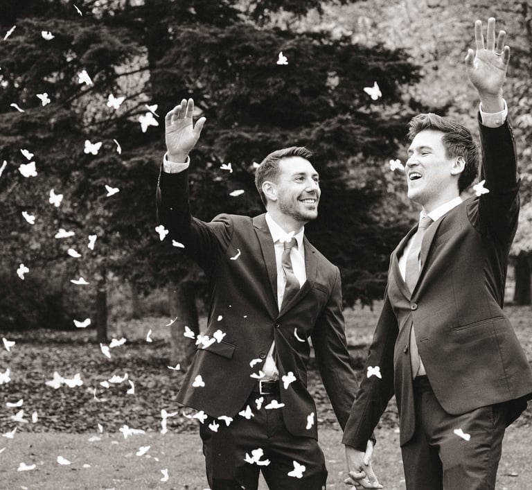 Pareja de recién casados gays sonriendo y lanzando pétalos de rosa mientras se toman de la mano. Gay wedding celebration.