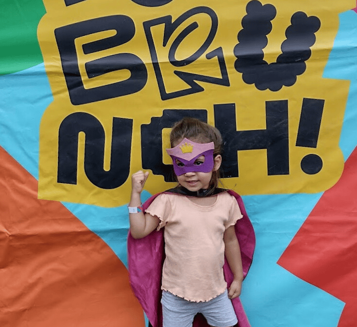 a little girl in a pink capelet and a pink capelet, behind text "brunch" in the petit brunch event
