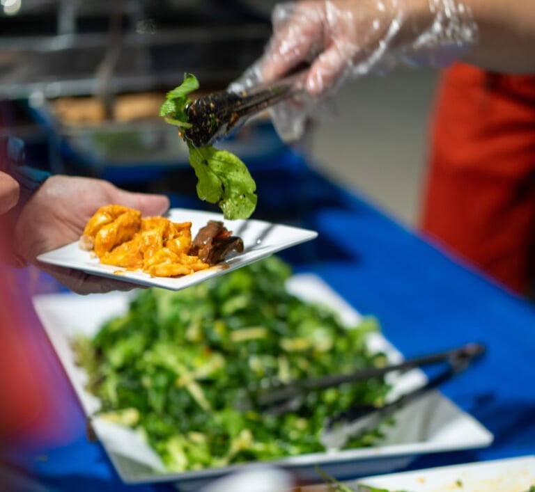 Hand serving salad with tongs onto a plate someone else is holding