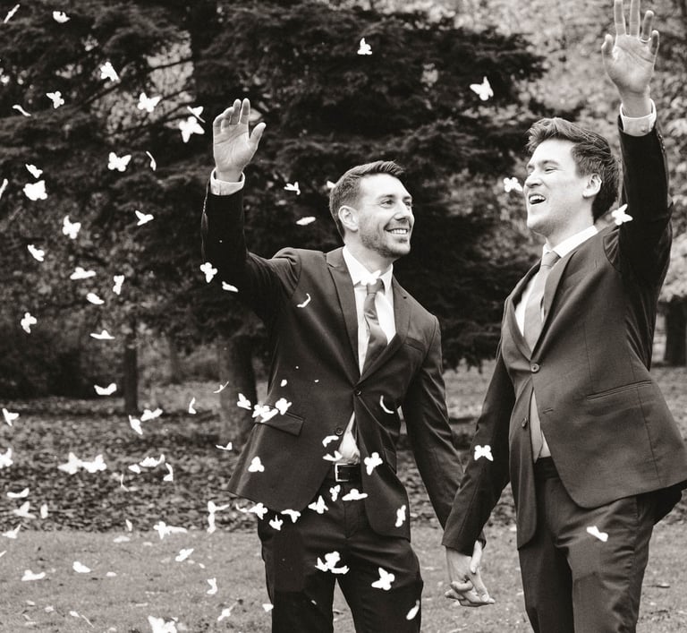 Pareja de recién casados gays sonriendo y lanzando pétalos de rosa mientras se toman de la mano. Gay wedding celebration.