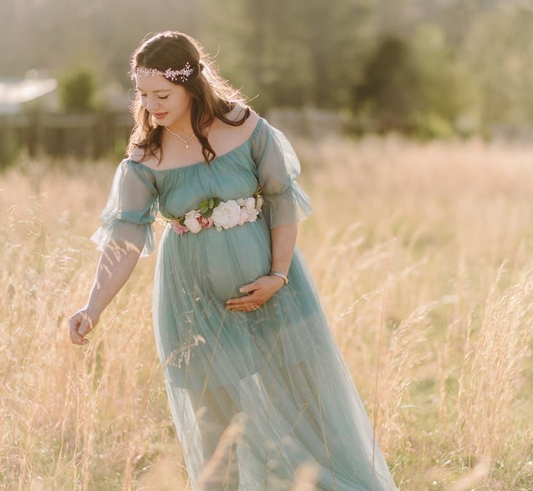 a pregnant woman in a blue dress standing in a field