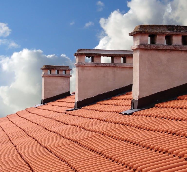 clay roof shingles with 3 white chimneys with a  blue sky background and clouds