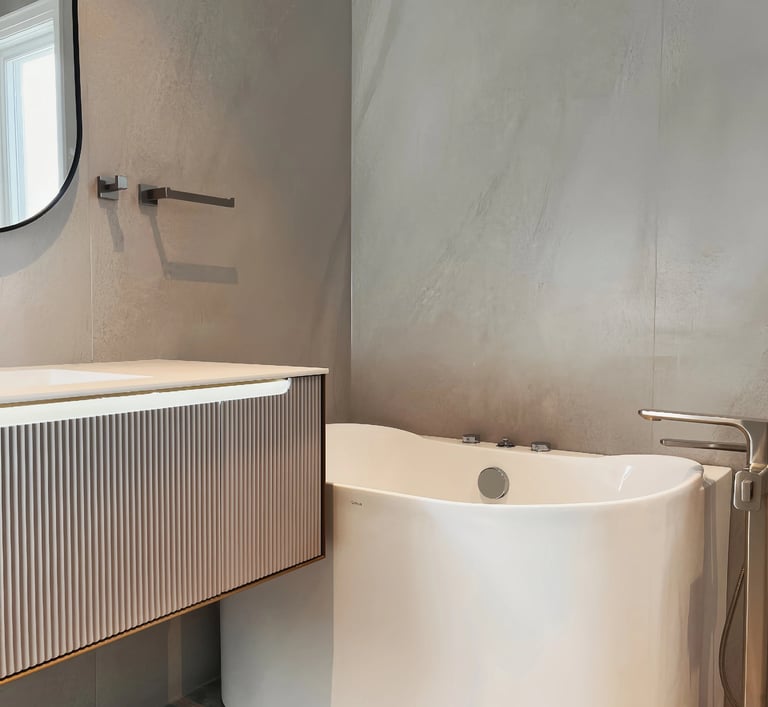 Modern bathroom interior featuring a white freestanding bathtub and fluted vanity cabinet against gray textured walls.