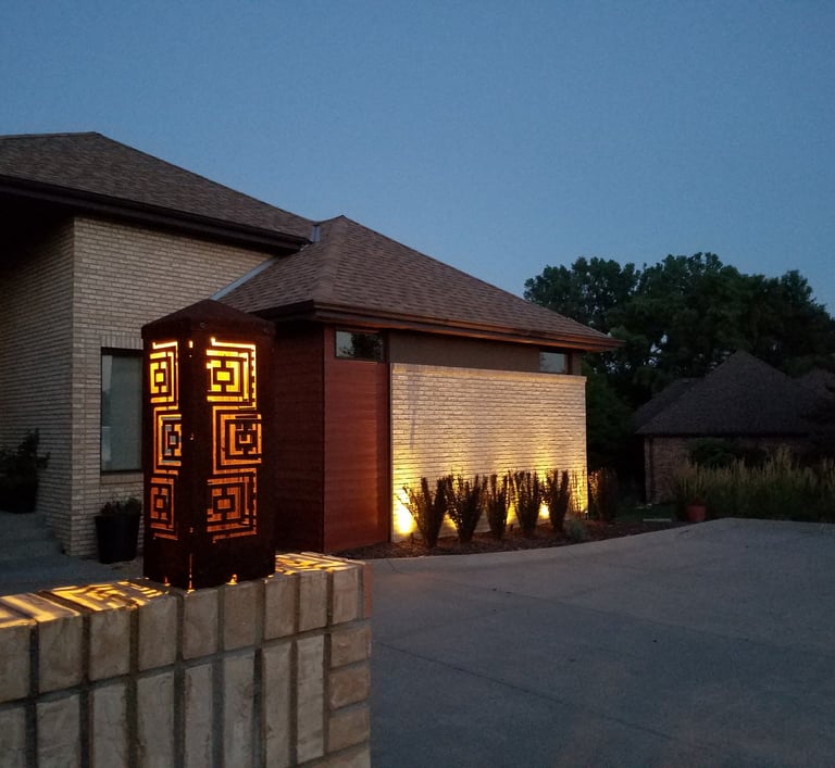 Modern outdoor landscape lighting illuminates a brick driveway and house exterior at dusk.