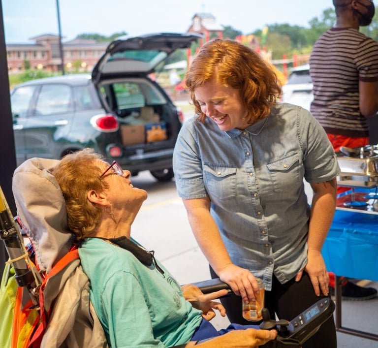Person in wheelchair talking and smiling up at someone standing talking to them