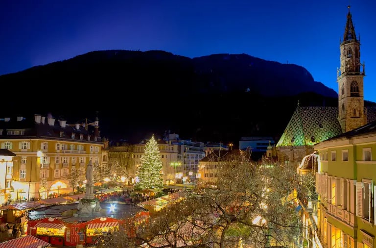 Bolzano Christmas Market at night with the Cathedral of Bolzano and mountains in the background