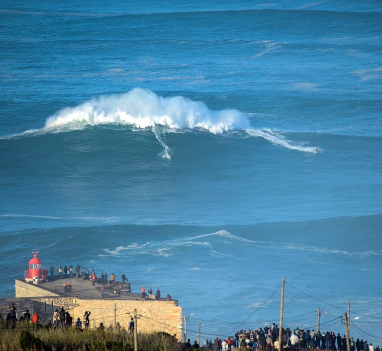 a large wave coming in to shore with people standing on the beach
