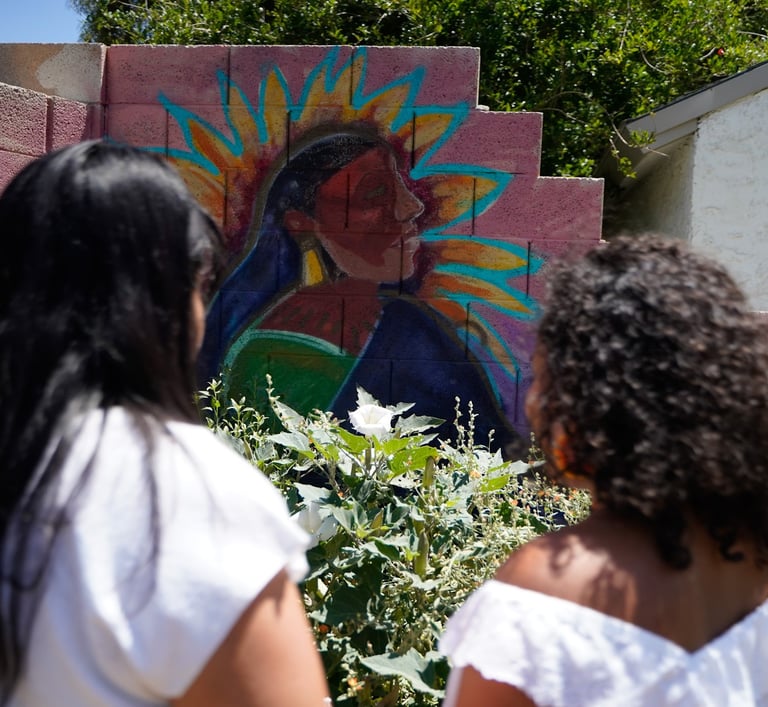 Iveth and Victoria standing in front of a Tonantzin's painting at the Giving Garden
