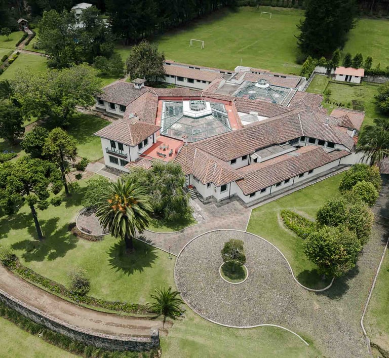 Fotografía con dron de mansión colonial de paredes blancas con techo naranja, cúpulas rodeada de naturaleza Quito Ecuador