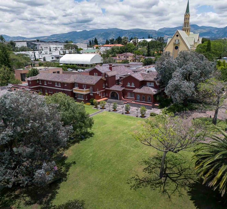 Fotografía aérea de gran casa religiosa de color rojo rodeada de hermoso jardín verde en Quito Ecuador