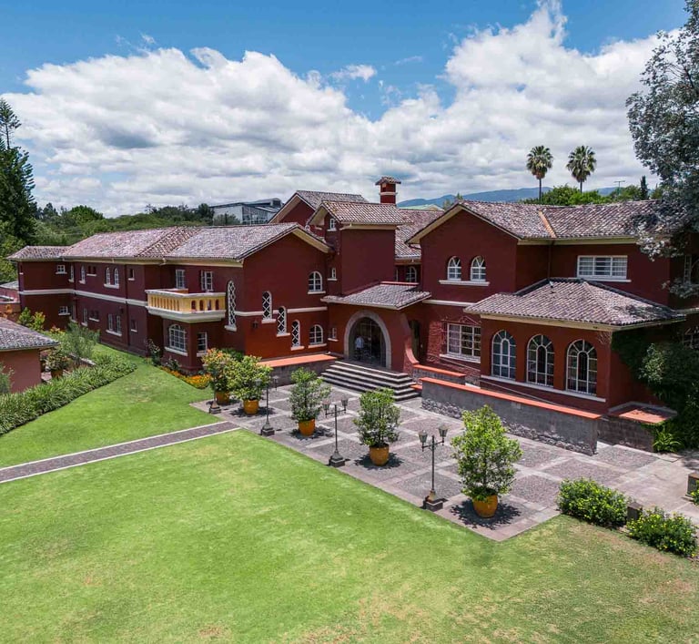 Fotografía aérea de gran casa religiosa de color rojo rodeada de hermoso jardín verde en Quito Ecuador