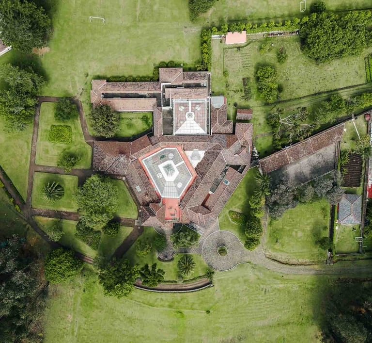 Fotografía con dron de mansión colonial de paredes blancas con techo naranja, cúpulas rodeada de naturaleza Quito Ecuador