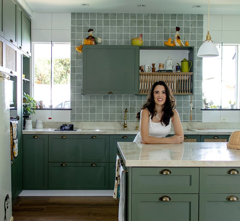 Foto da arquiteta Luciana em uma cozinha clássica com marcenaria verde, bancada de pedra natural e muita iluminação natural