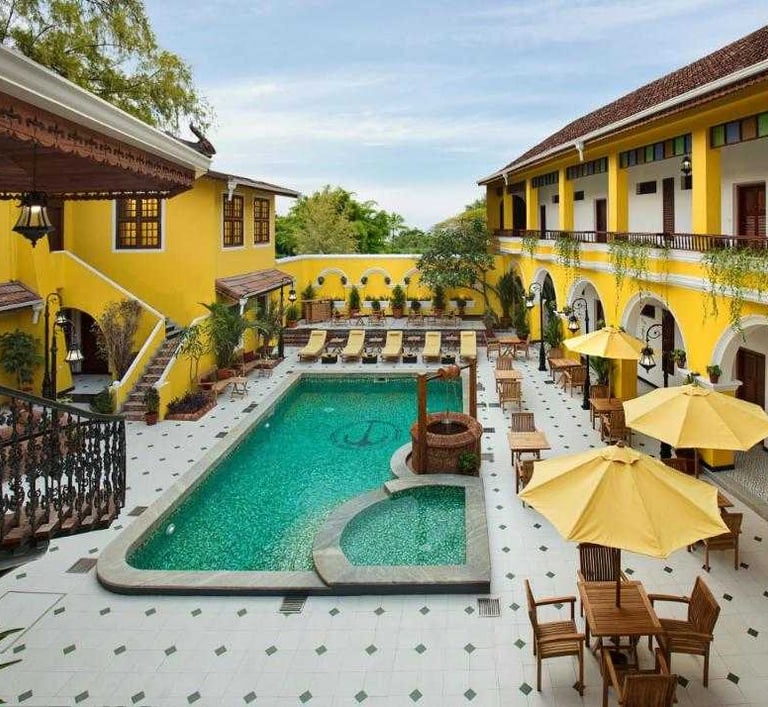 Charming resort in Fort Kochi, Kerala, featuring a vibrant yellow facade, a serene swimming pool, sun loungers, and umbrellas