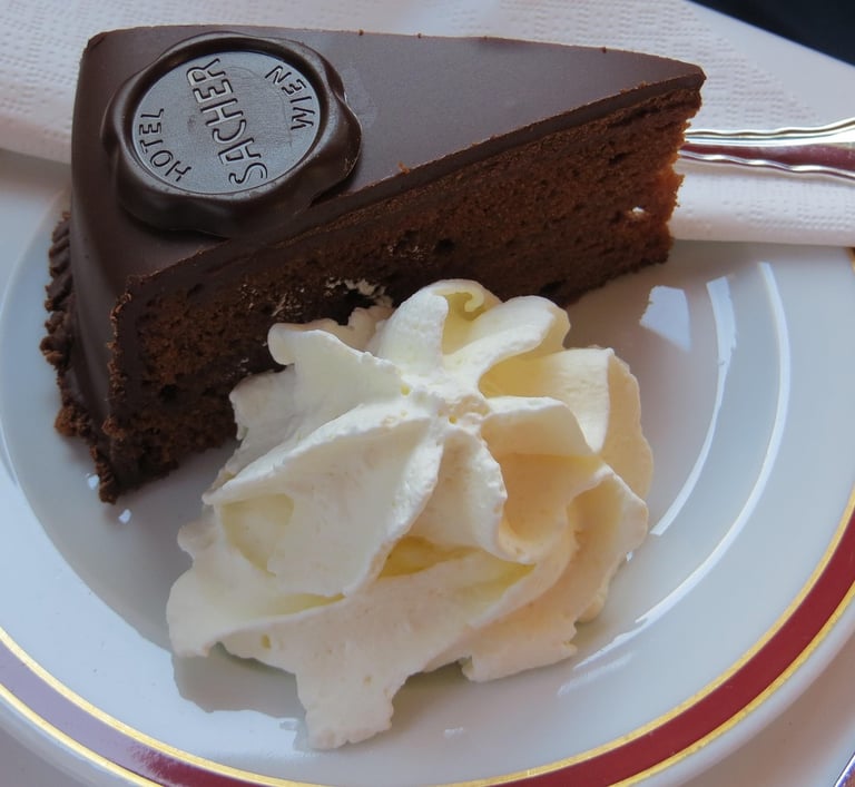 Porción de tarta Sacher con su sello oficial de chocolate y una guarnición de nata montada