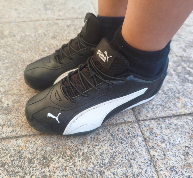 Criança a usar as sapatilhas infantis Puma Catch pretas e brancas num chão de calçada