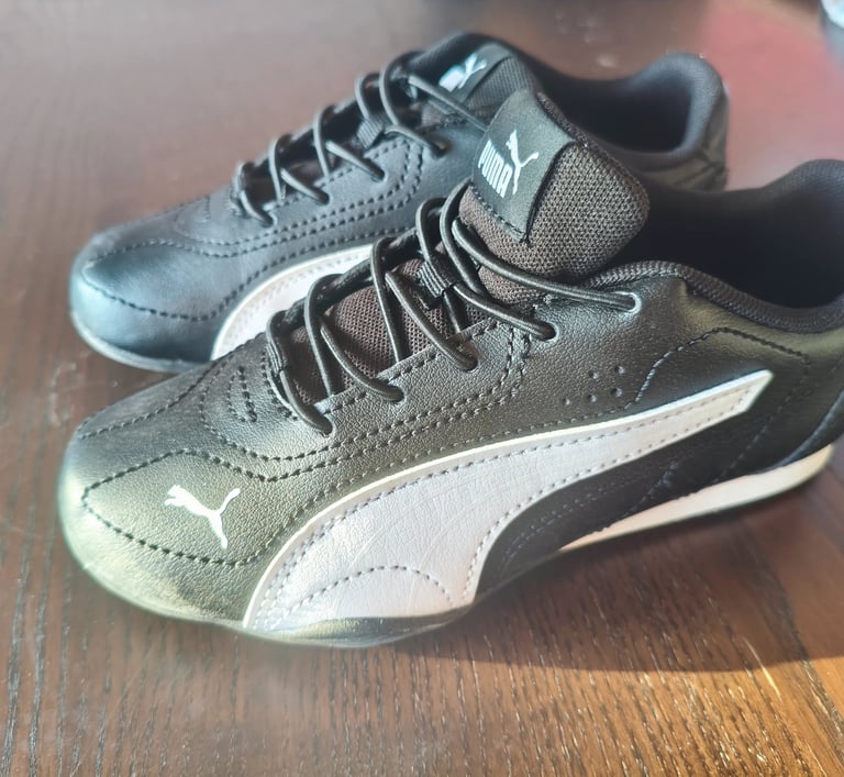 Sapatilhas infantis Puma Catch pretas e brancas vistas de lado em cima de uma mesa de madeira