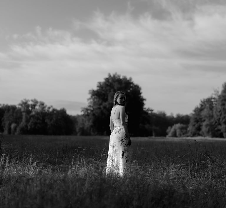 Black and white outdoor portrait of a woman in a floral maxi dress standing in a grassy field.