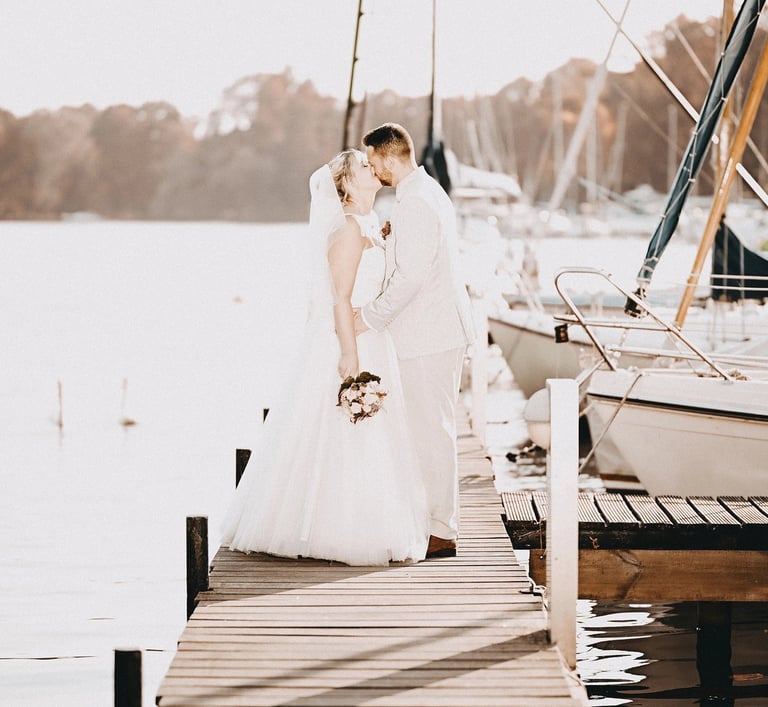 Brautpaar küsst sich auf einem Steg am Möhnesee bei Sonnenlicht – romantischer Moment eingefangen vom Hochzeitsfotografen am 
