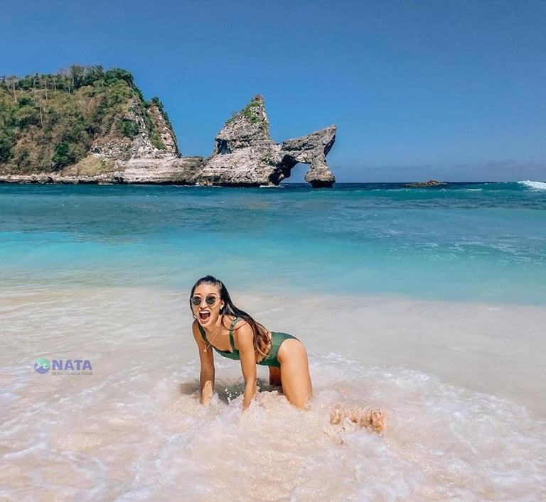 A woman in a swimsuit posing on Atuh Beach with the iconic rock formation in Nusa Penida.