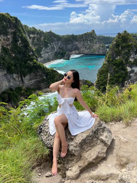 A woman in a white dress posing at Diamond Beach viewpoint in Nusa Penida, Bali.