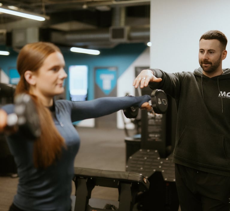Client doing lateral dumbbell raise in Leamington Spa gym, coached by trainer focused on form and shoulder activation
