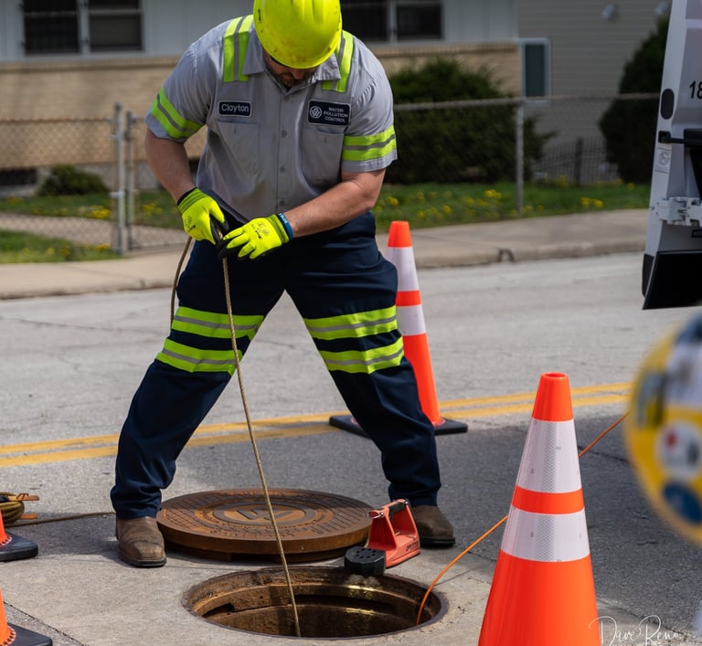 Public Works worker in safety gear accessing a sewer manhole as part of routine maintenance operations.