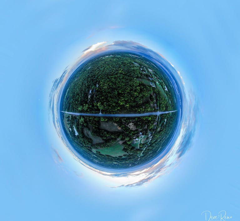 Spherical aerial panorama of a forested landscape with a straight road cutting across a small planet at dusk.